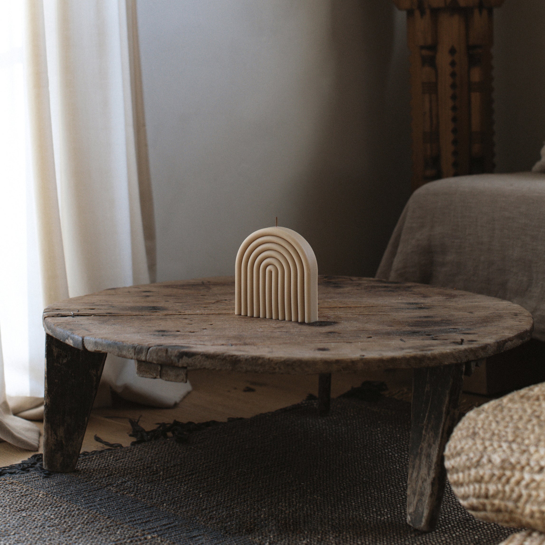 LAWA sandstone rainbow pillar candle featuring warm sculptural arches on Wooden table with a decorative arch sculpture in a room setting