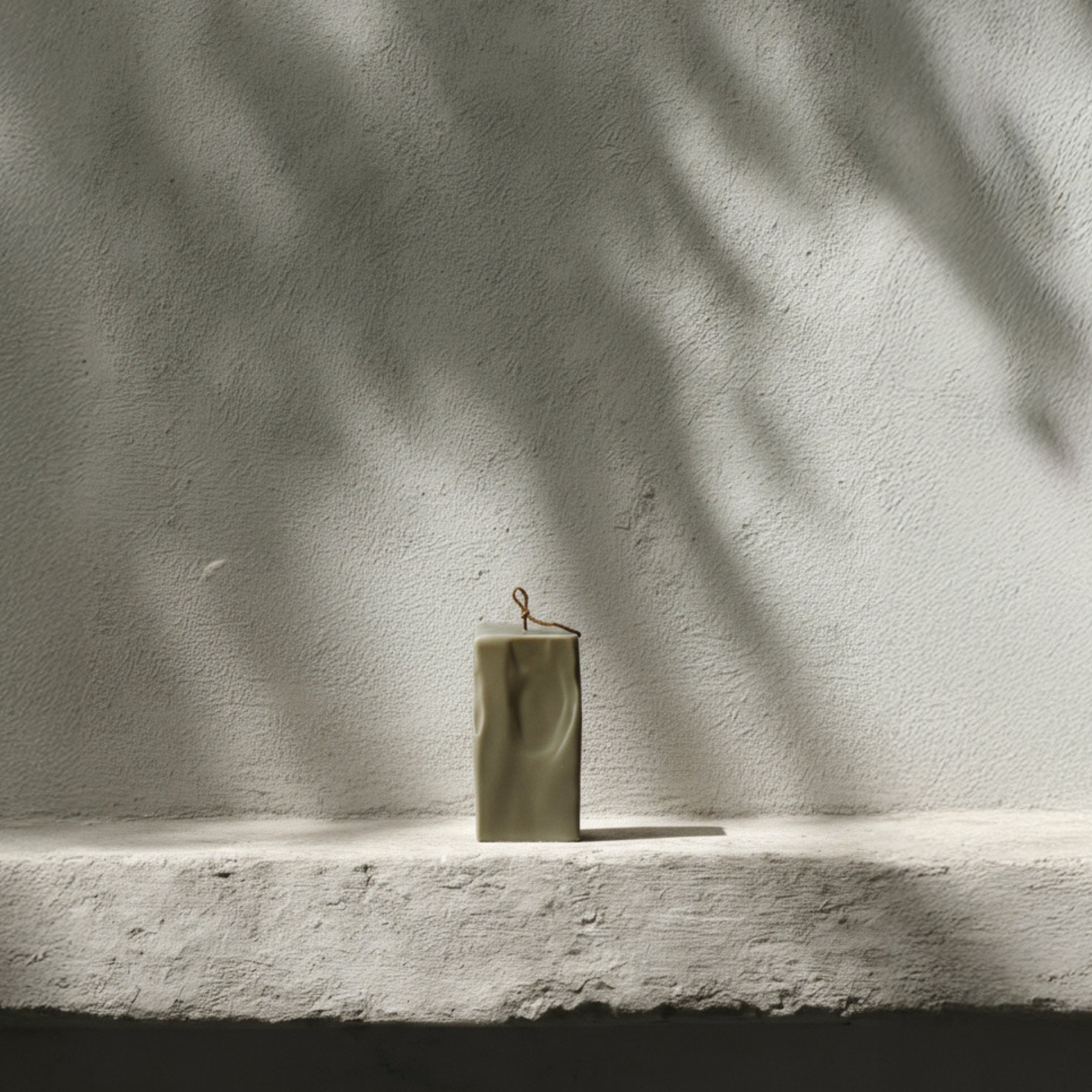 Large earthy green raw block candle by LAWA on a textured surface with shadows cast by leaves.