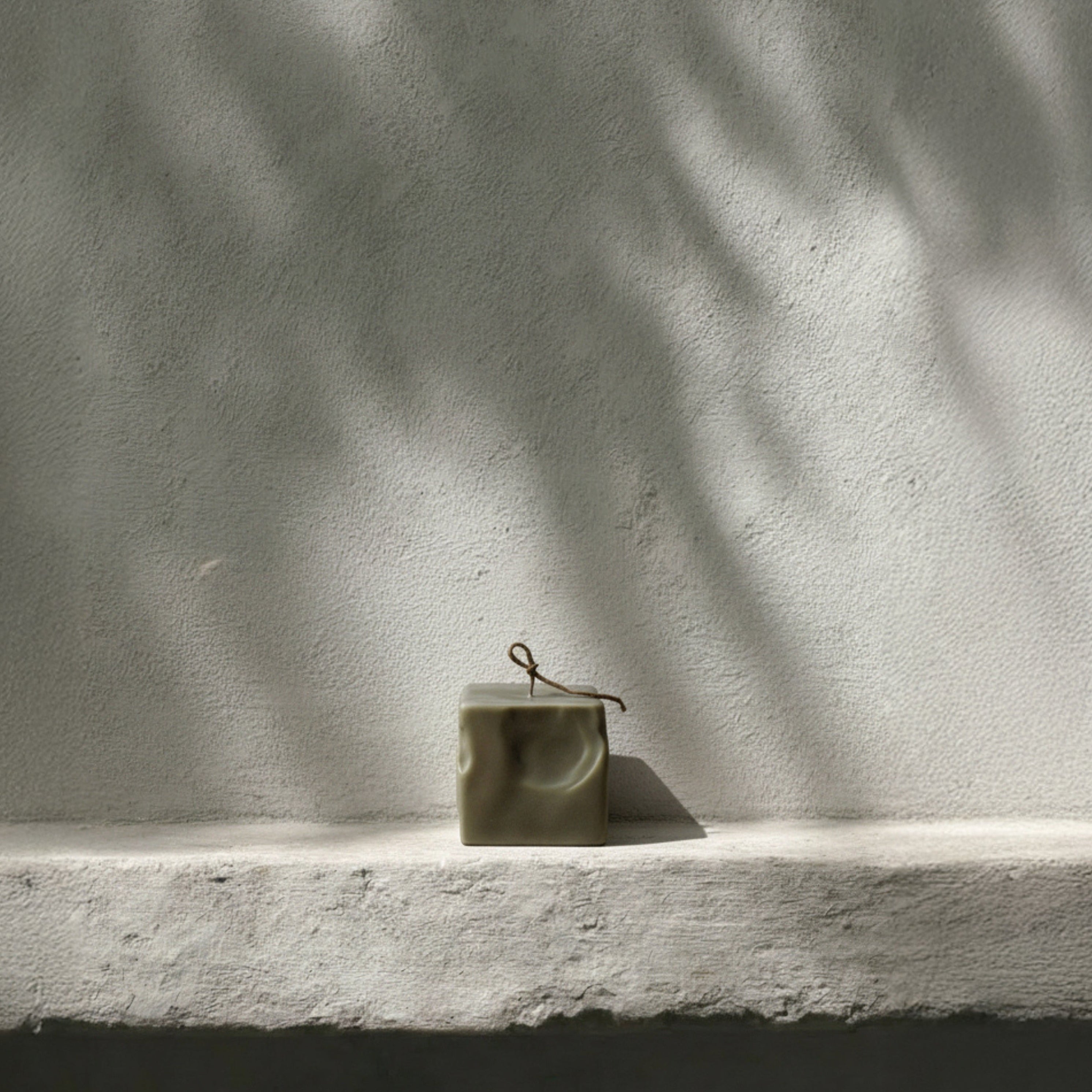 LAWA small raw block candle in earthy green on a white surface with a textured gray wall background