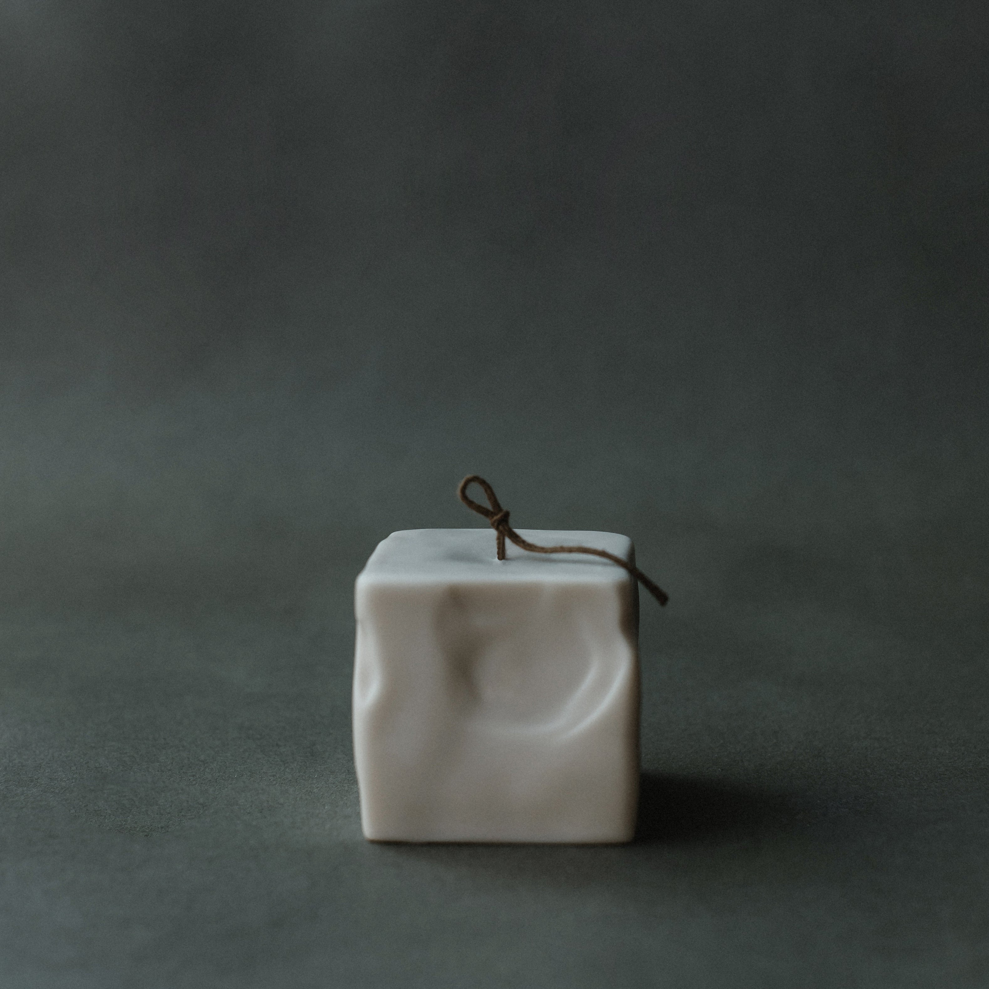 Small light beige raw block candle by LAWA with minimalist rectangular sculptural form on a dark green background