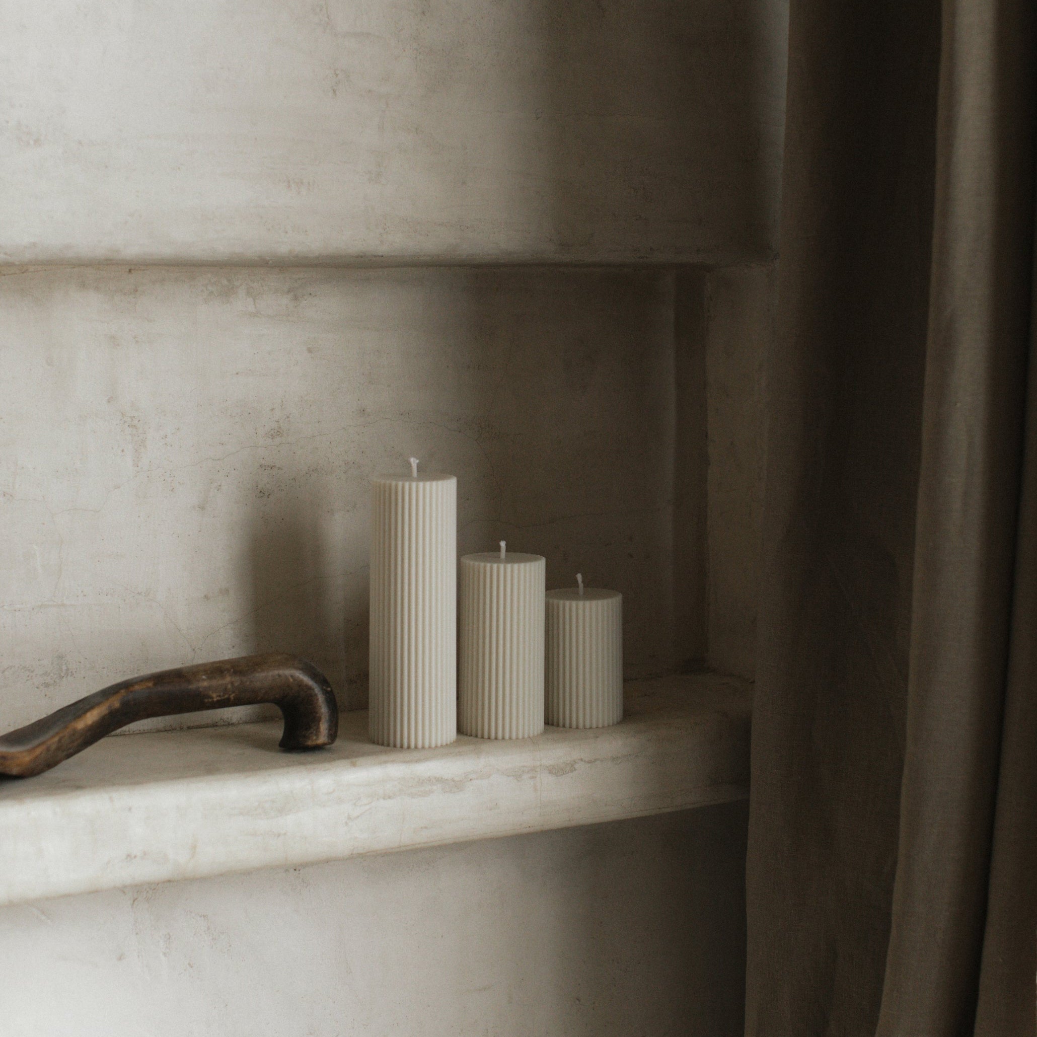 Three ribbed pillar candles on a marble shelf with a neutral background