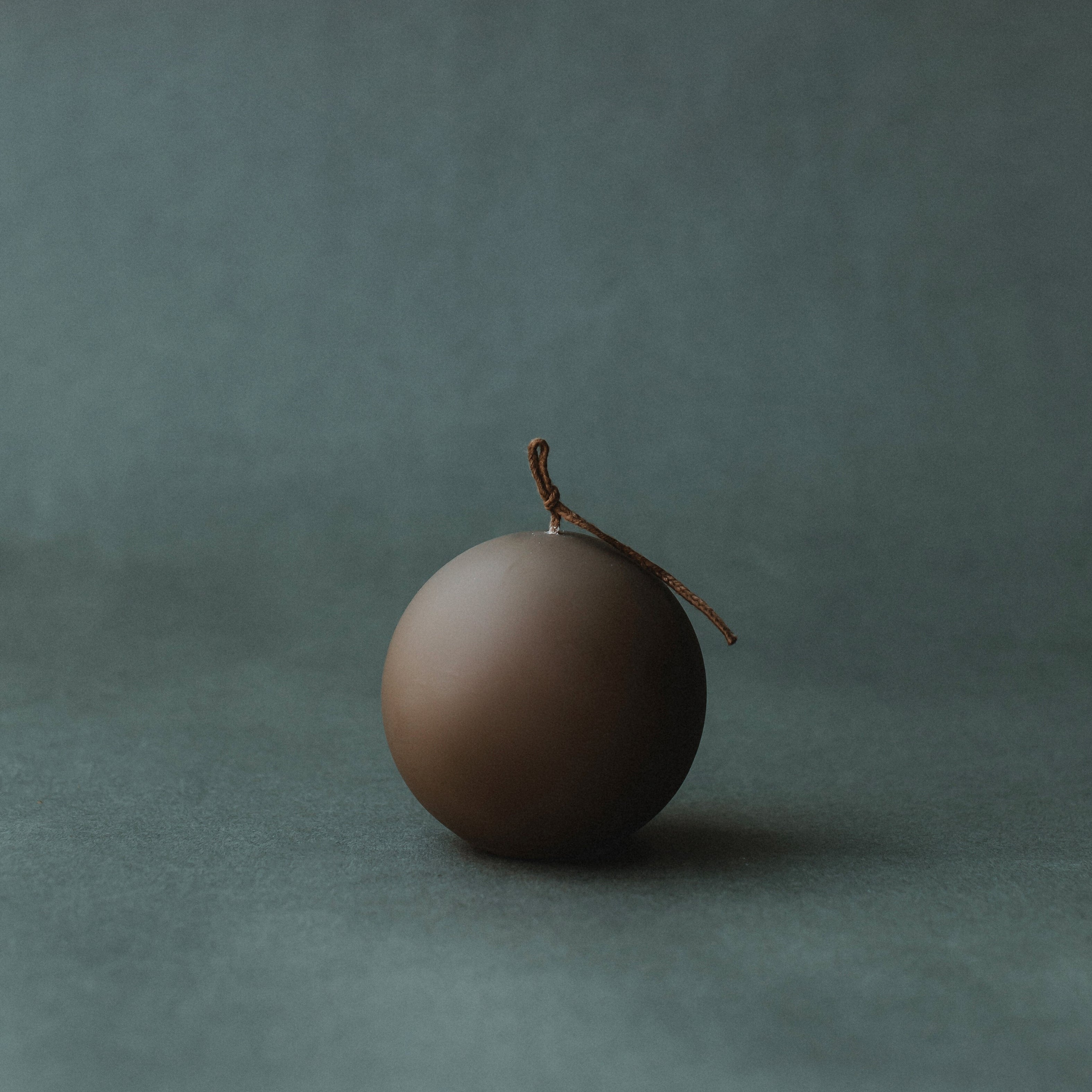 Kobicha brown sphere pillar candle on a dark green background
