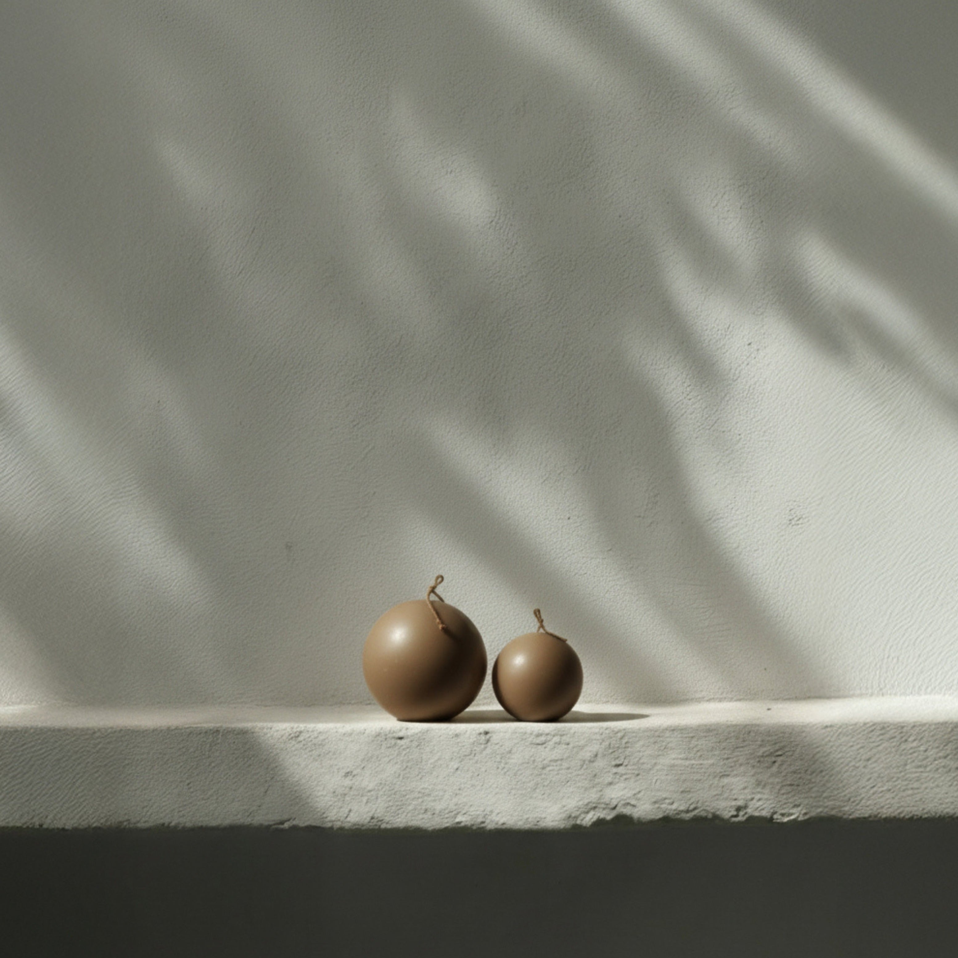 Kobicha brown sphere pillar candles on a light surface with a shadow pattern on the wall.