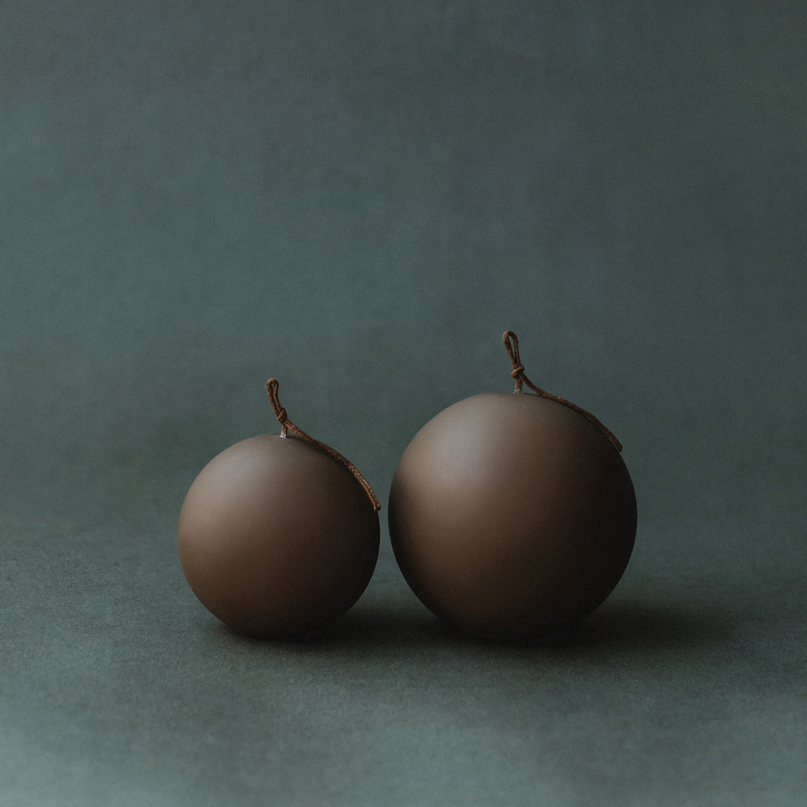 Two kobicha brown  pillar spherical candles on a dark green background