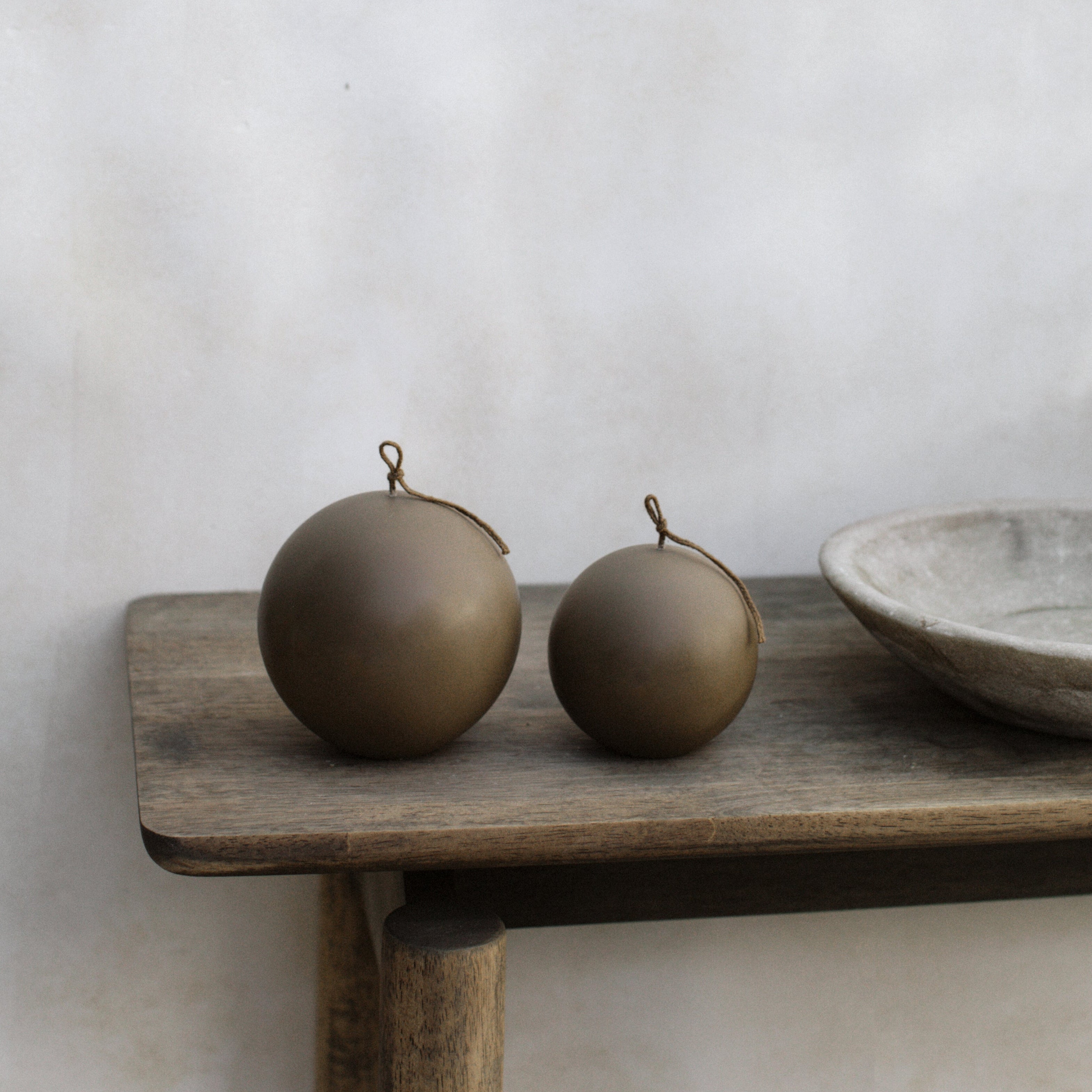 Kobicha brown set of two sphere candles on a wooden shelf against a plain wall.
