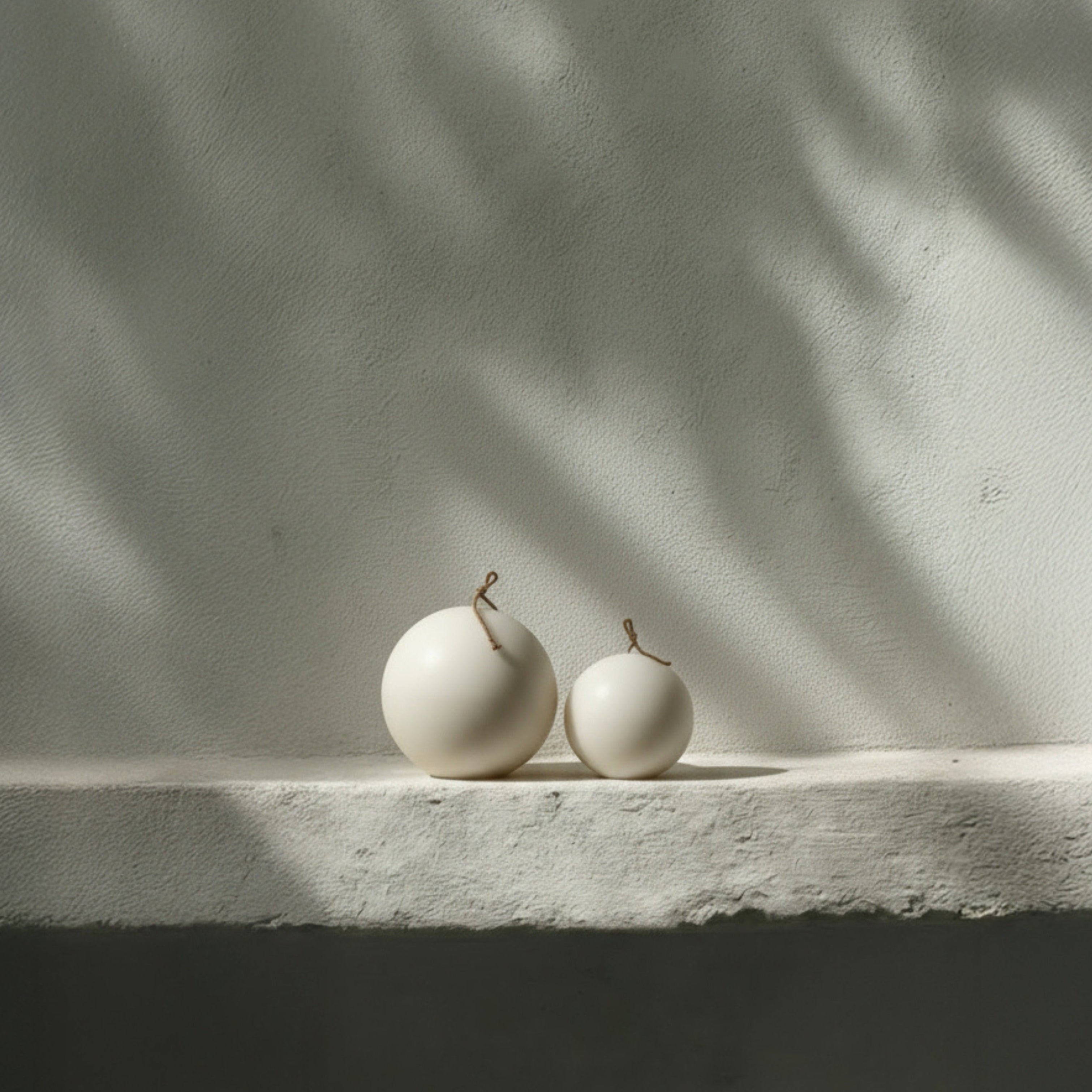Two light beige sphere pillar candles on a stone surface with a neutral background