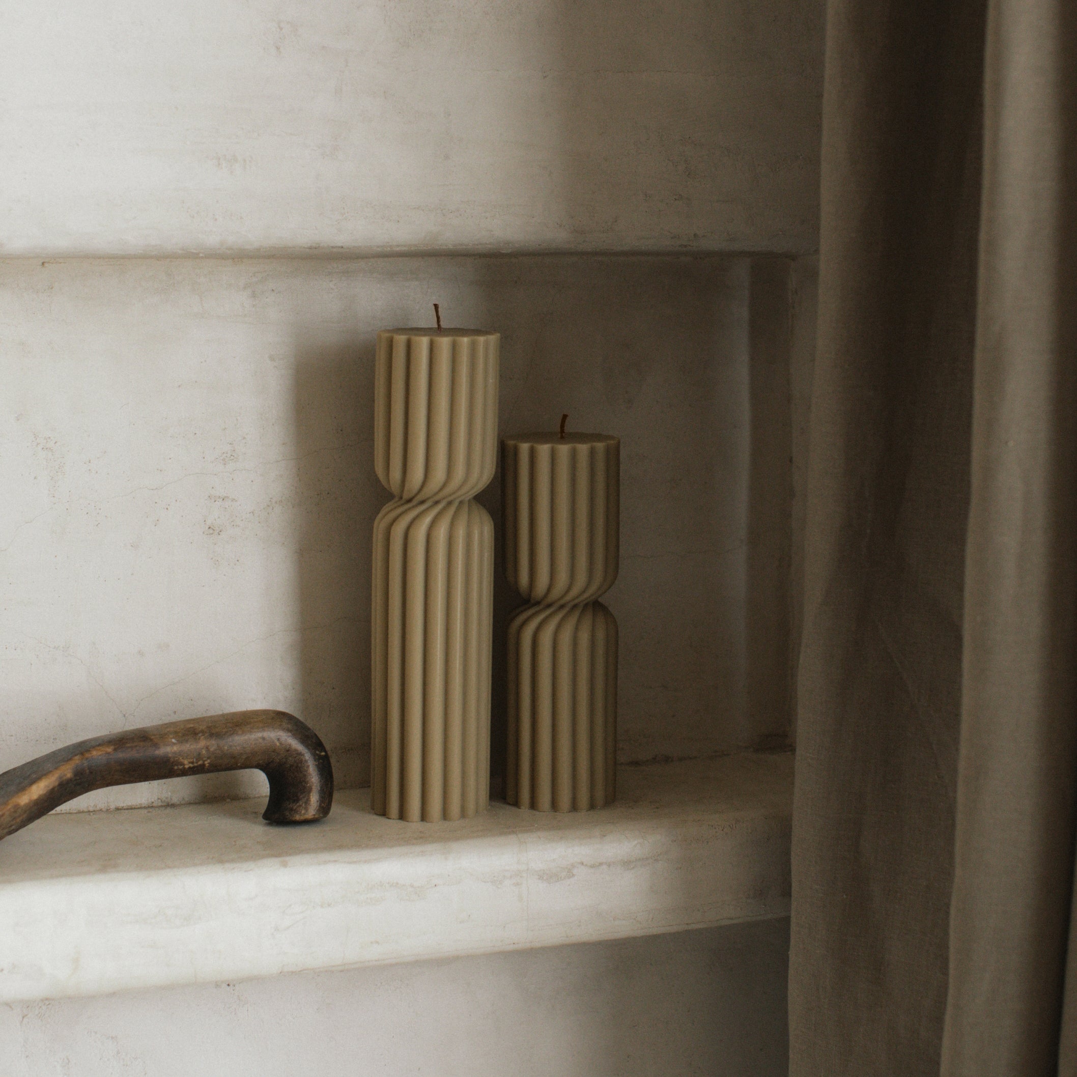 Olive beige sculptural spiral pillar candle duo on a marble shelf with a neutral background
