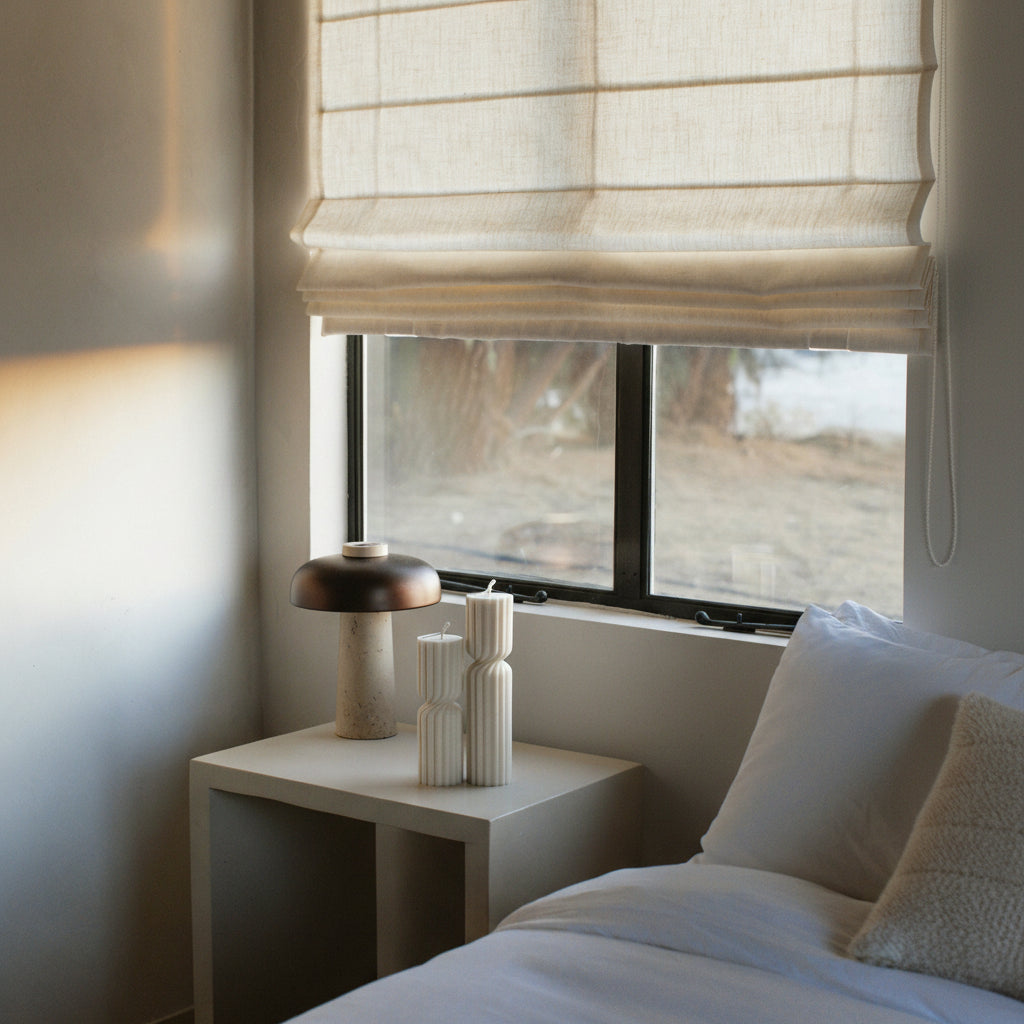 White spiral set of two pillar candles in a bedroom with a window, nightstand, and bed.