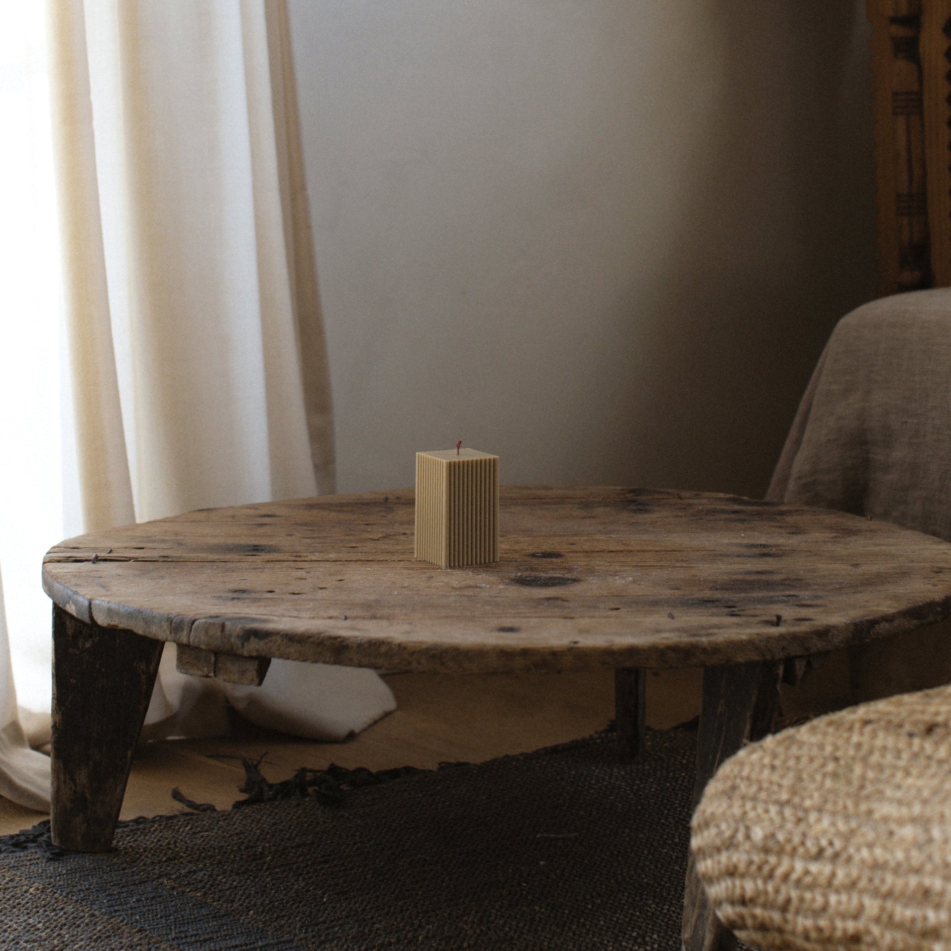 Olive beige ribbed pillar candle by LAWA featuring structured minimal grooves on a wooden coffee table with a textured surface in a room setting.