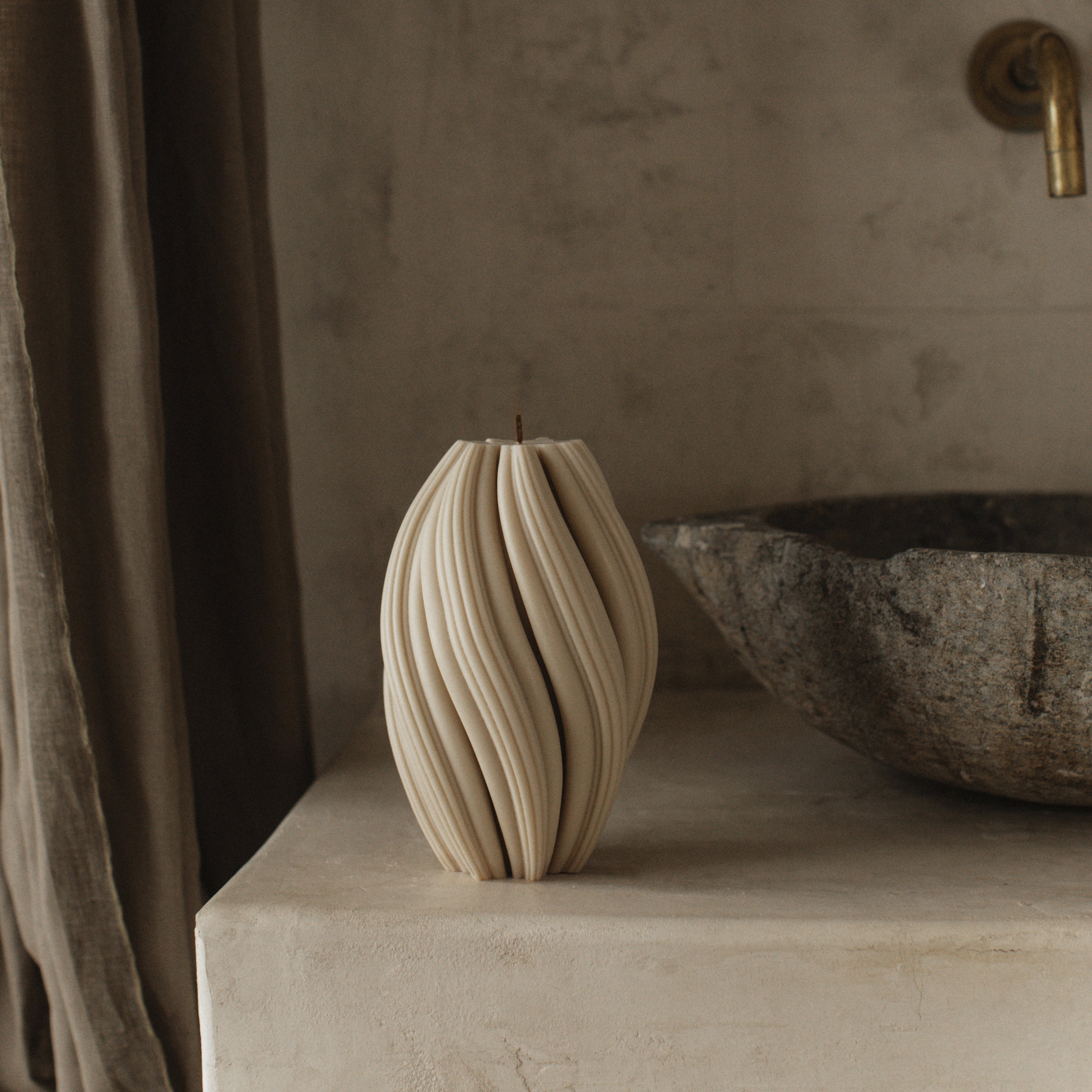 Moon gray large swirl pillar candle by LAWA with elegant spiraling silhouette on a stone surface with a textured wall and curtain in the background