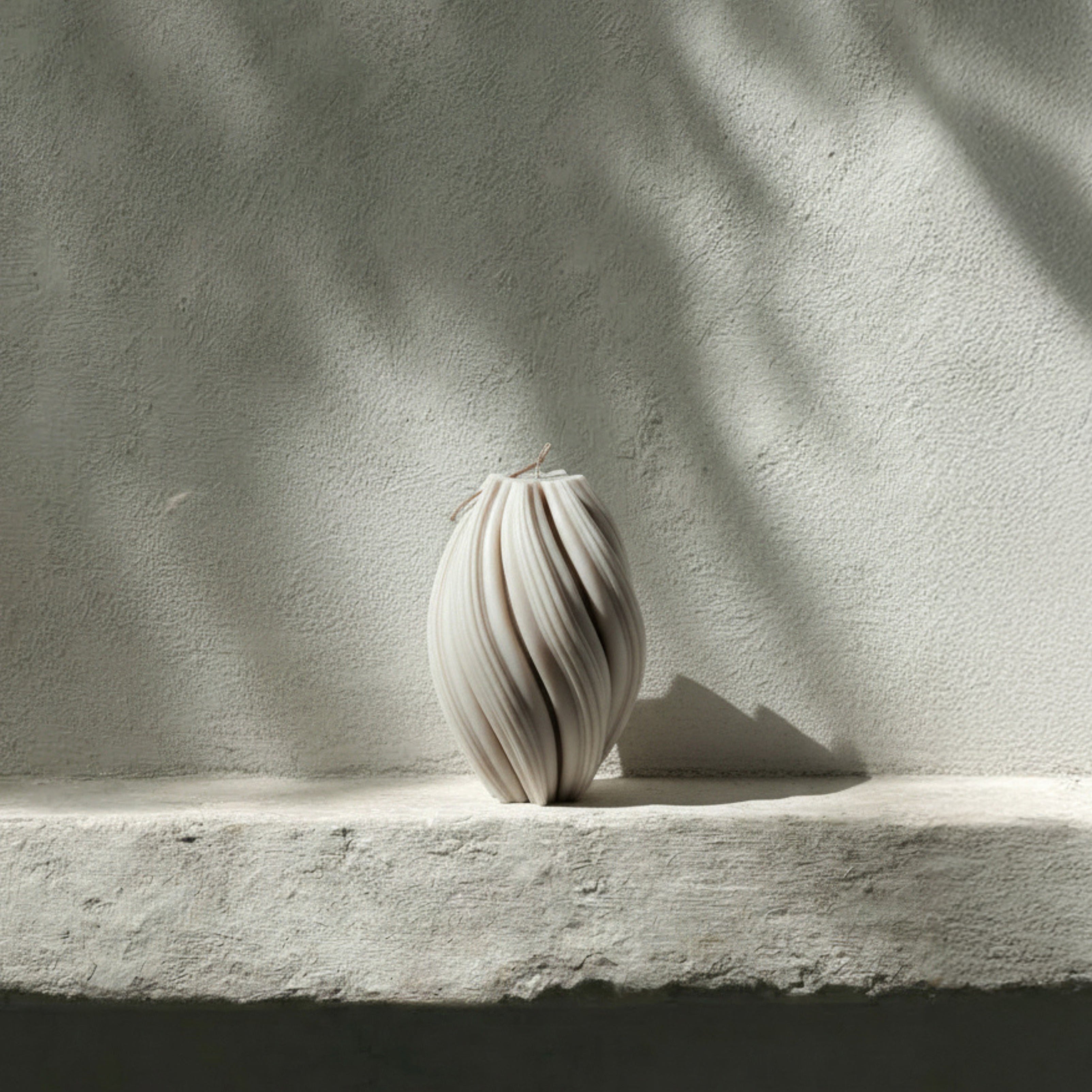 White large swirl pillar candle by LAWA with elegant curved swirling design on a textured stone surface with soft shadows
