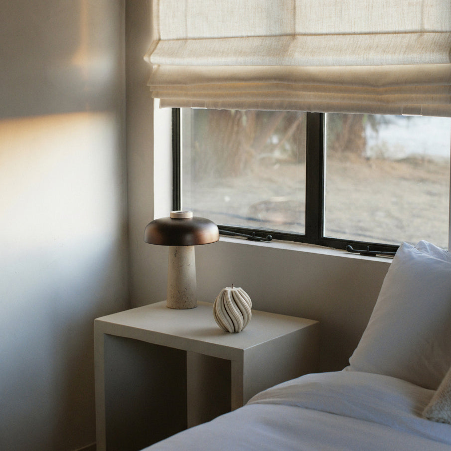 LAWA medium swirl candle in moon gray featuring soft twisted texture in a Modern bedroom with a side table, lamp near a window.