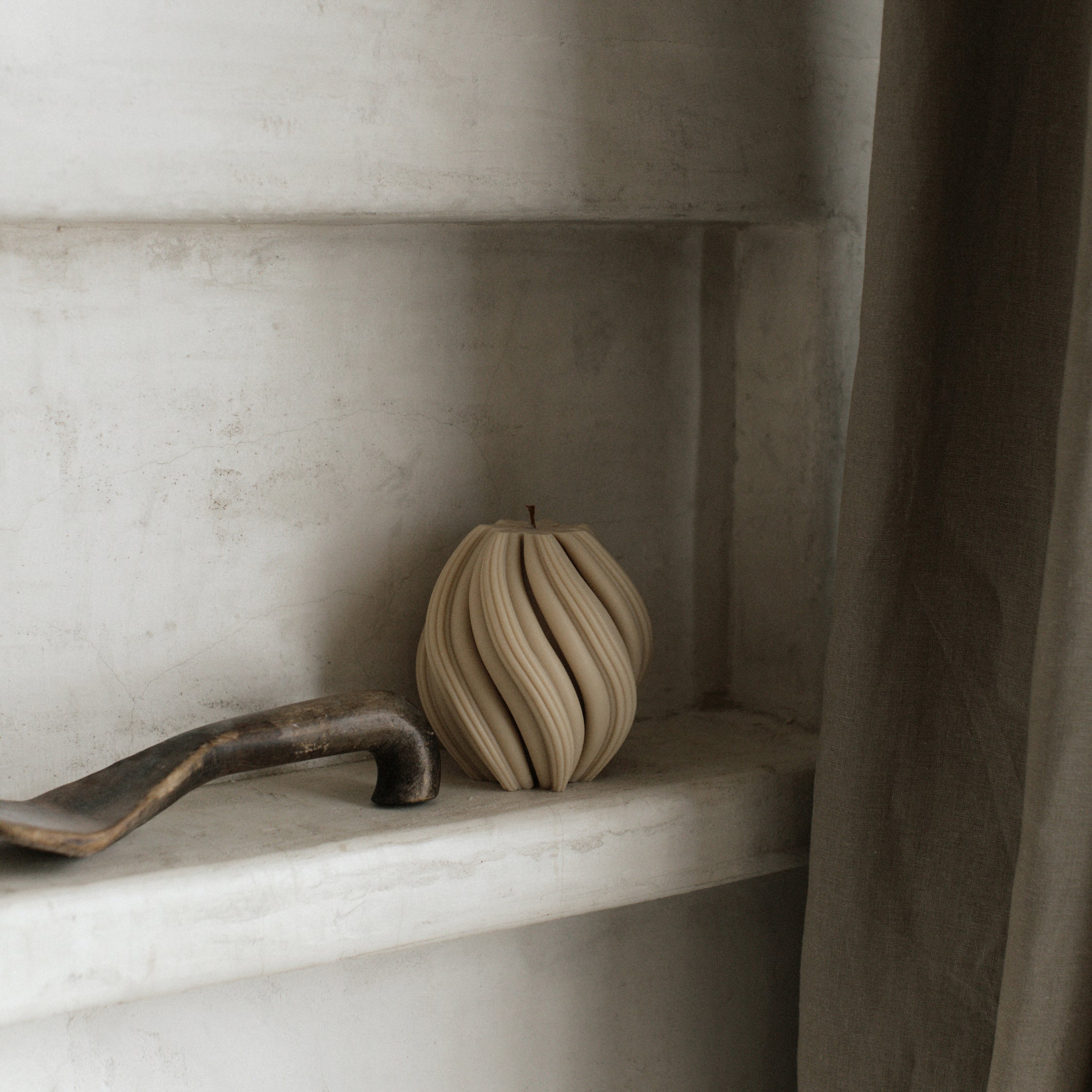 Sandstone medium swirl pillar candle by LAWA with smooth twisted silhouette  on a shelf against a neutral wall