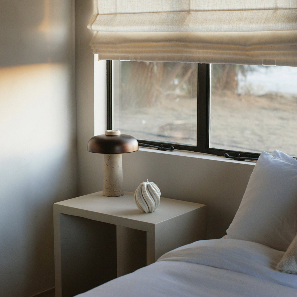 LAWA medium swirl candle in white featuring modern spiral texture in a Bedroom with a nightstand, lamp, and window with blinds.