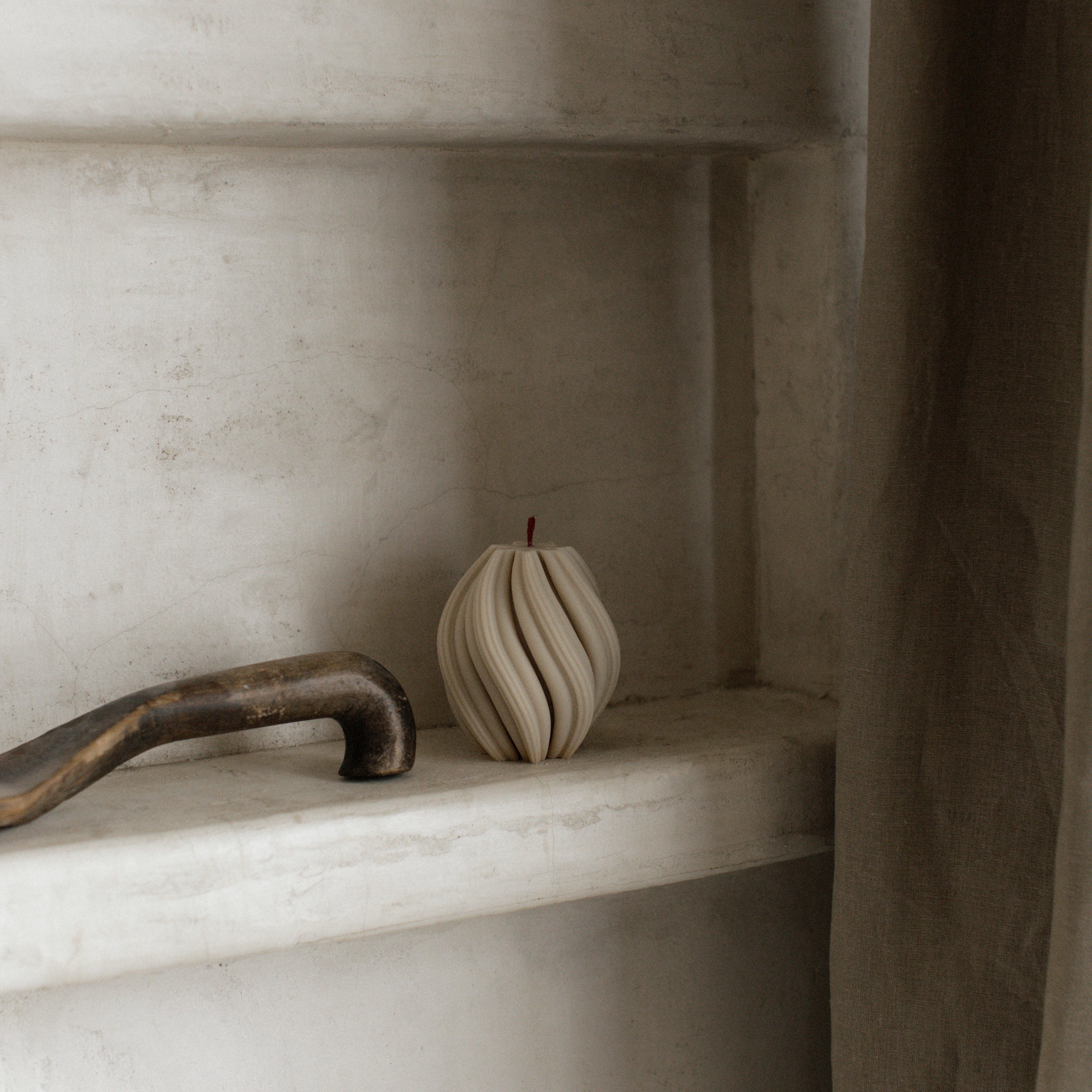 Minimal small swirl pillar candle in moon gray by LAWA with smooth curved detailing on a marble shelf with a rustic handle.