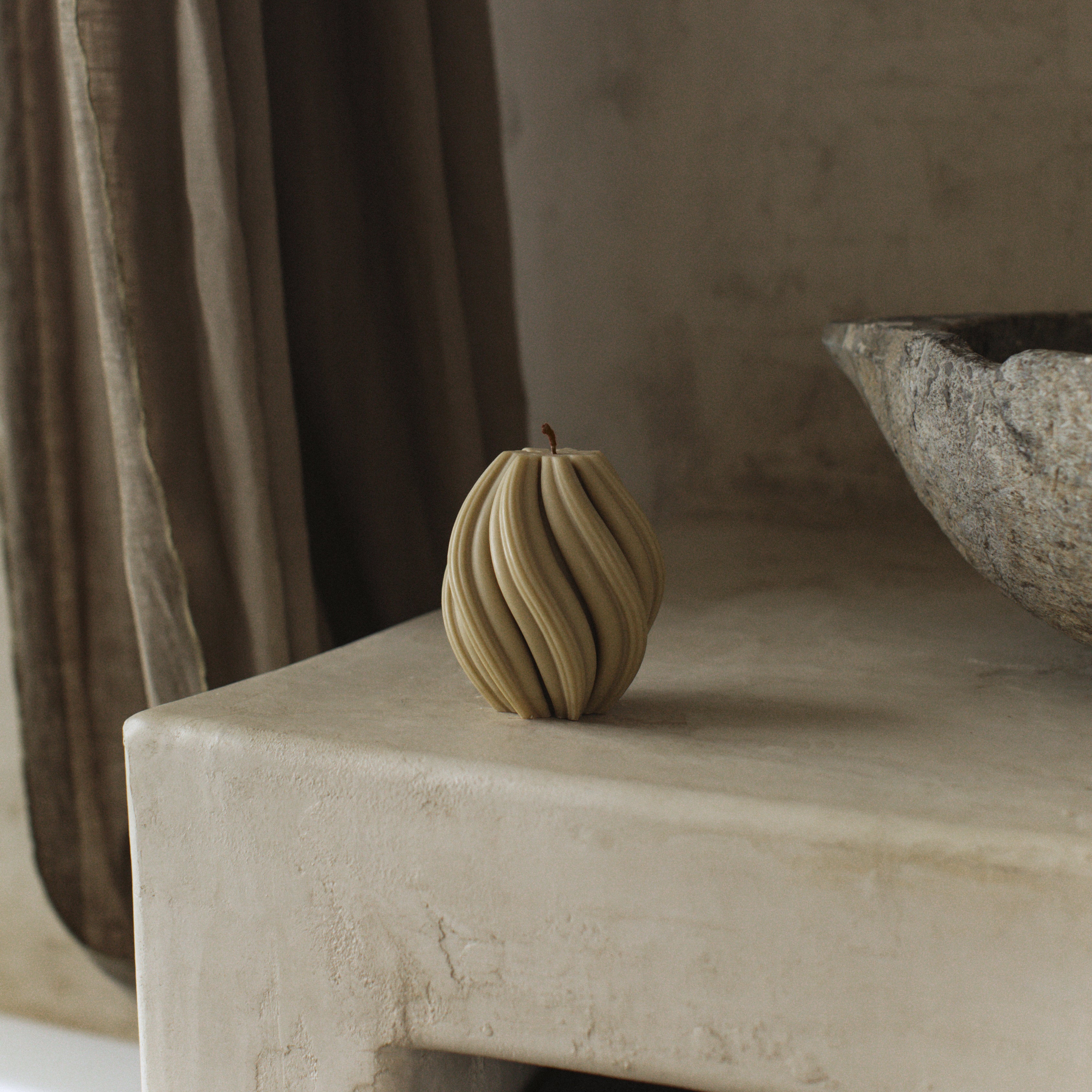 Minimalist small olive beige swirl pillar candle by LAWA with soft twisted detailing on a stone surface with a neutral background
