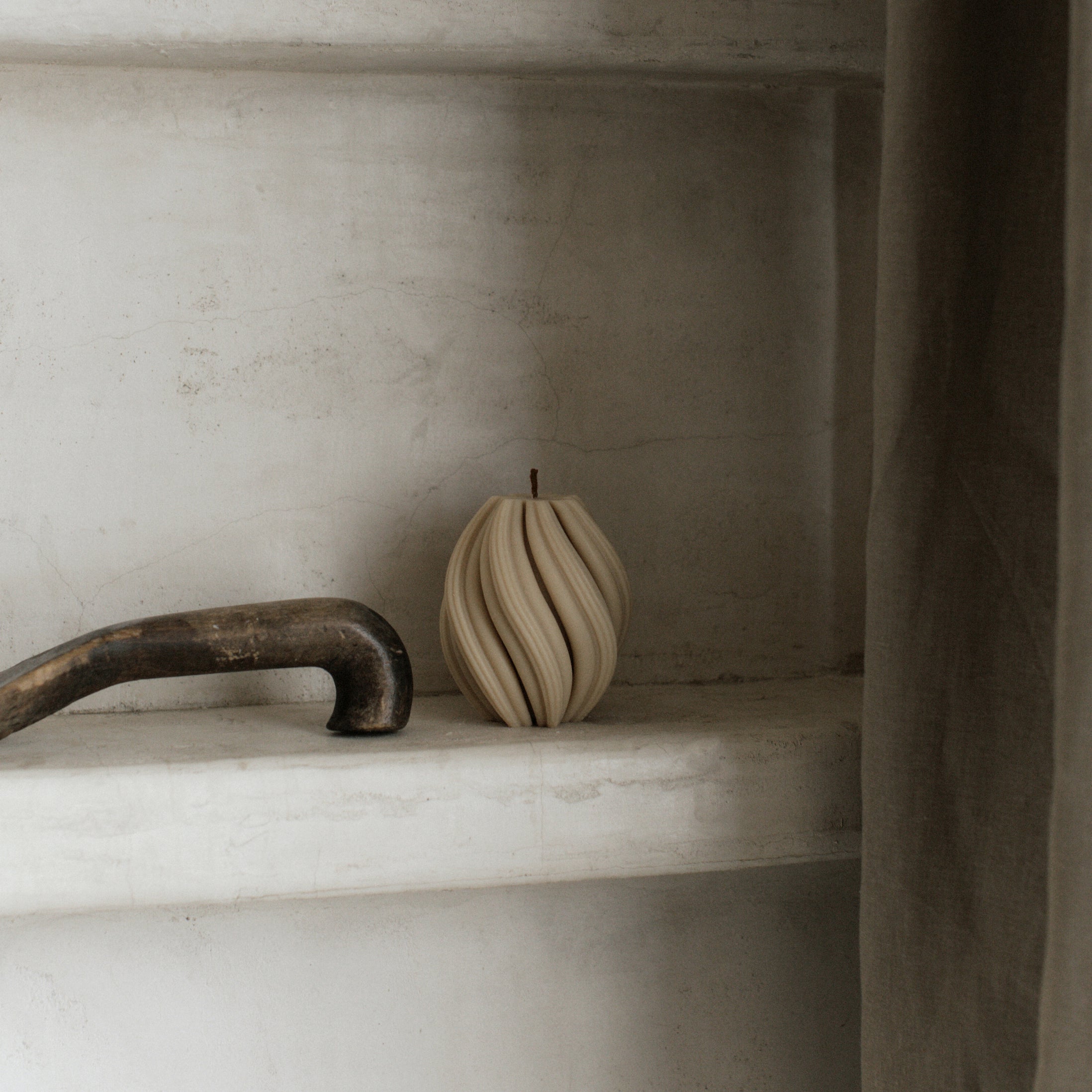 Minimal small sandstone swirl pillar candle by LAWA with elegant curved design on a marble shelf with a rustic handle in the background