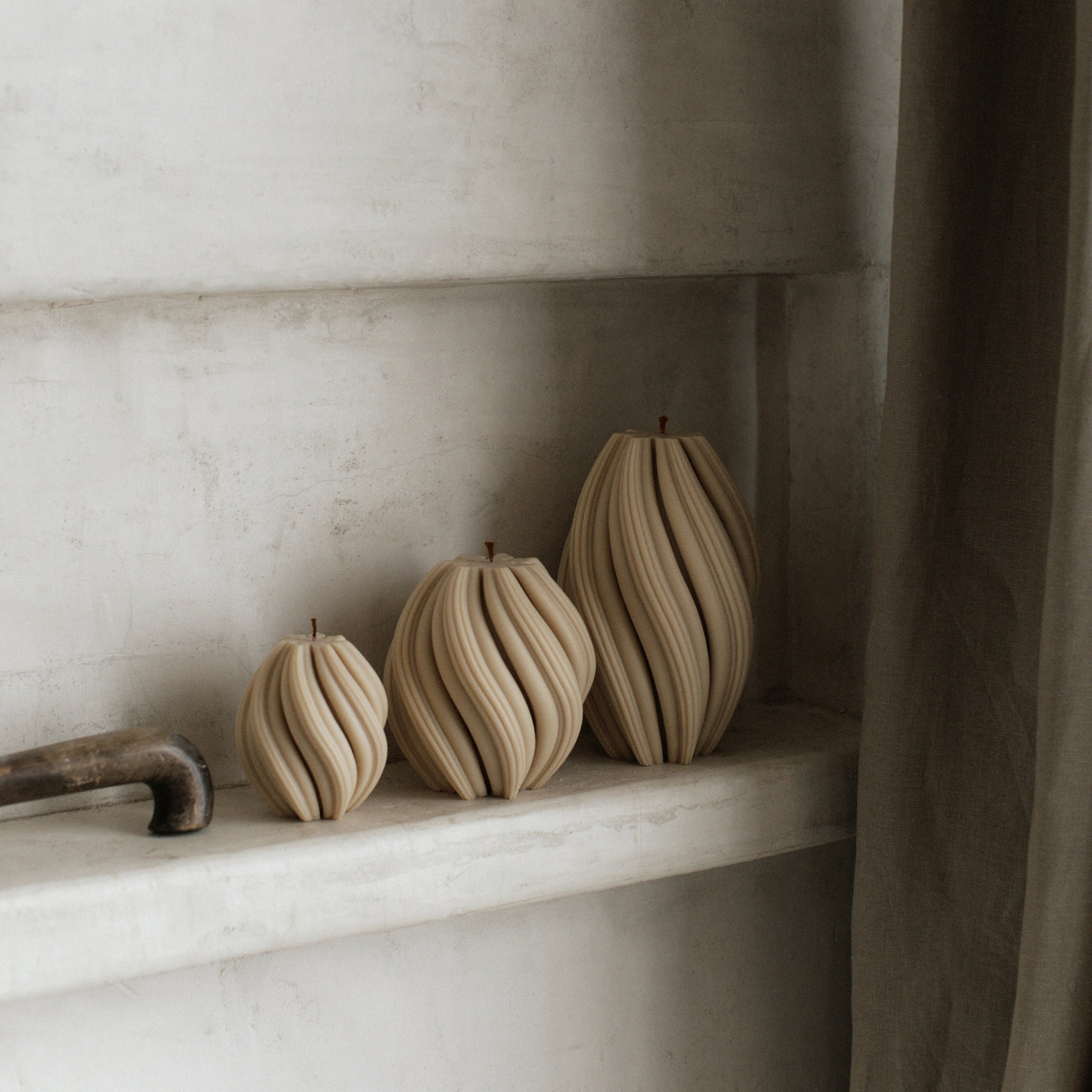 Sandstone soy wax swirl candle set of 3 by LAWA with modern twisted spiral silhouettes on a shelf against a neutral wall.