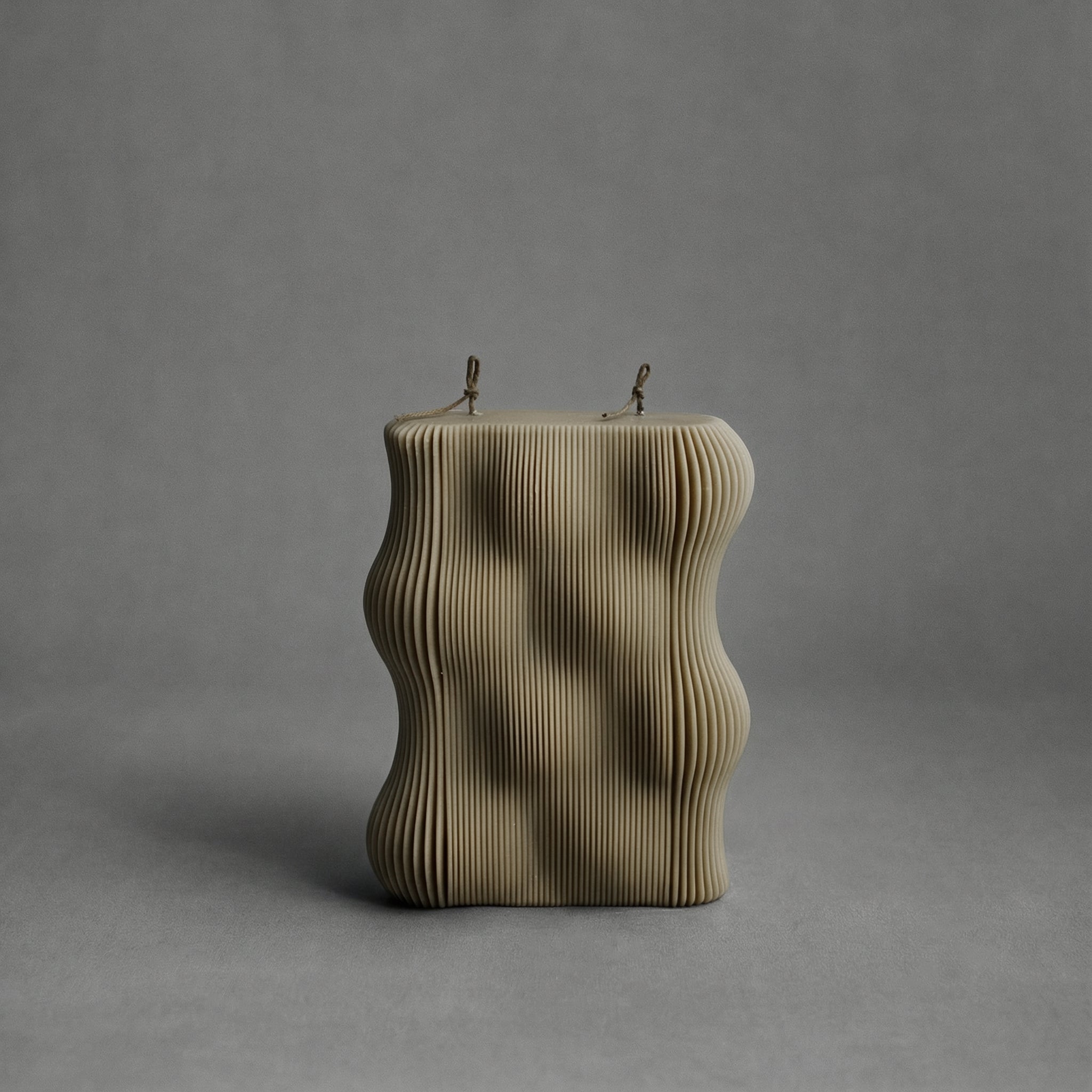 Olive beige wavy pillar candle on a gray background