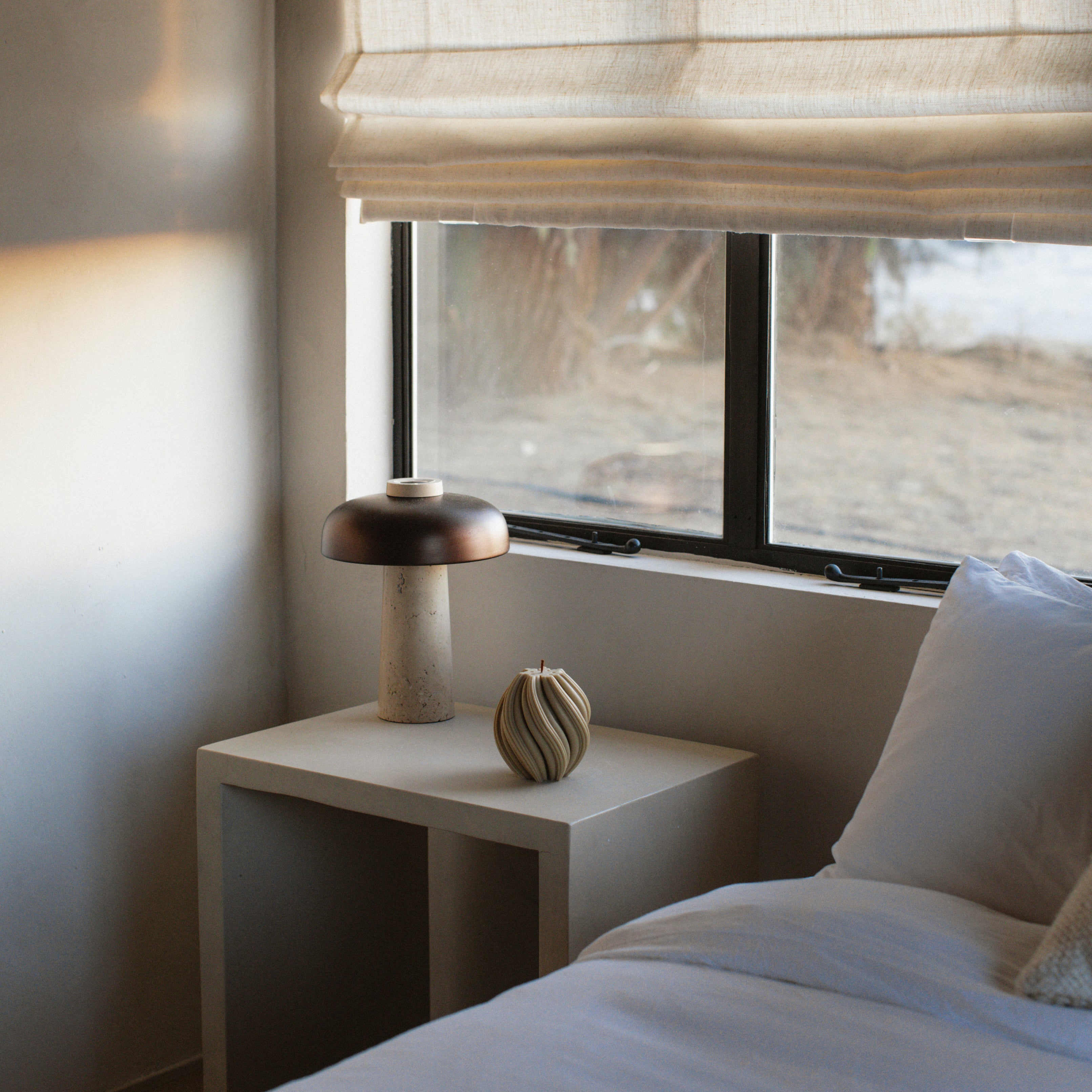 LAWA medium swirl pillar candle in olive beige with modern spiral texture on a nightstand next to a bed with white bedding.
